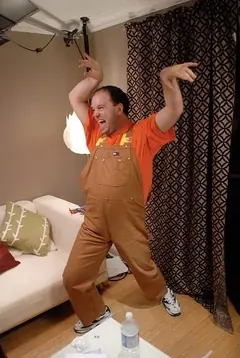 Adrian Gorrissen in brown overalls and an orange shirt, raising both arms.